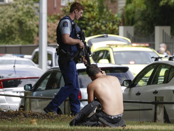 FILE - A man rests on the ground while speaking on his mobile phone as a police officer walks near the Al Noor mosque following a mass shooting March 15, 2019, in central Christchurch, New Zealand. Su ...