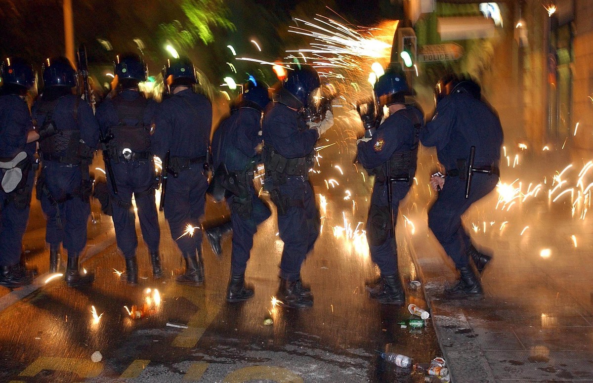 Swiss riot police take cover from exploding fireworks fired at them during riots in downtown Geneva, Monday June 2, 2003. Hundreds of anti-G-8-demonstrators were locked up on Geneva's main bridge ...