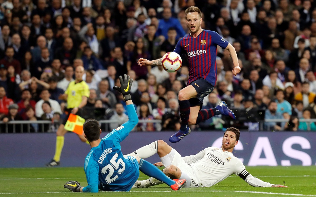 epa07409553 FC Barcelona's Ivan Rakitic (top) beats Real Madrid's goalkeeper Thibaut Courtois (bottom) and Sergio Ramos (R) to score the 0-1 lead during a Spanish LaLiga soccer match between ...