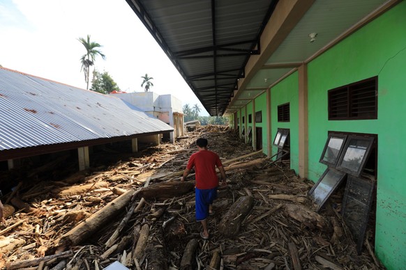 epa12566118 A person walks by an Islamic boarding school building that was damaged after being hit by swept away logs, at a flood-affected village in the Meureudu area of Pidie Jaya, Aceh, Indonesia,  ...