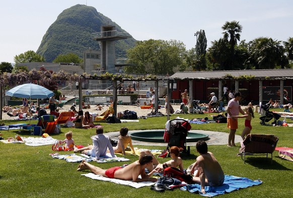 Sonnenhungrige vergnuegen sich am Freitag, 1. Mai 2009, bei Lufttemperaturen von ueber 20 Grad im Luganeser mit dem Monte San Salvatore im Hintergrund. Das Lido in Lugano wird taditionsgemaess am 1. M ...