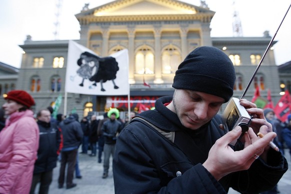 Manifestanten stehen mit Transparenten auf dem Bundesplatz, ein Mann hoert Radio, am 13. Dezember 2007. Rund 300 Leute versammelten sich am Morgen vor dem Bundeshaus als der Entscheid von Eveline Widm ...