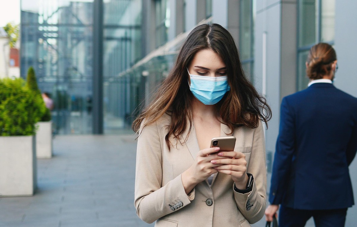 Frau mit Maske guckt auf Handy.