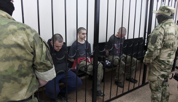 FILE - Two British citizens Aiden Aslin, left, and Shaun Pinner, right, and Moroccan Saaudun Brahim, center, sit behind bars in a courtroom in Donetsk, in the territory which is under the Government o ...