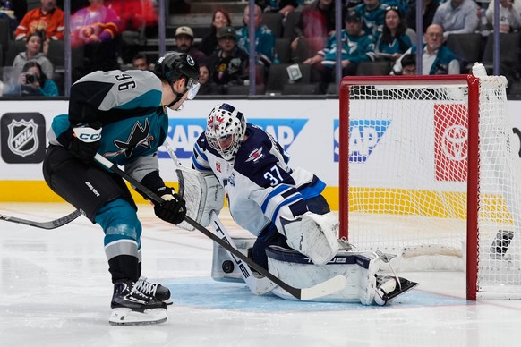 Winnipeg Jets goaltender Connor Hellebuyck (37) blocks a shot by San Jose Sharks center Philipp Kurashev (96) during the third period of an NHL hockey game, Sunday, March 1, 2026, in San Jose, Calif.  ...