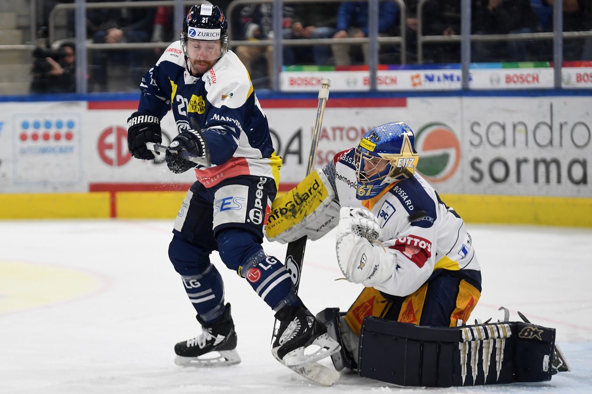 Ambri's player Brandon McMillan, left, fight for thr puck with Zug's goalkeeper Leonardo Genoni, right, during the preliminary round game of National League Swiss Championship 2021/22 betwee ...