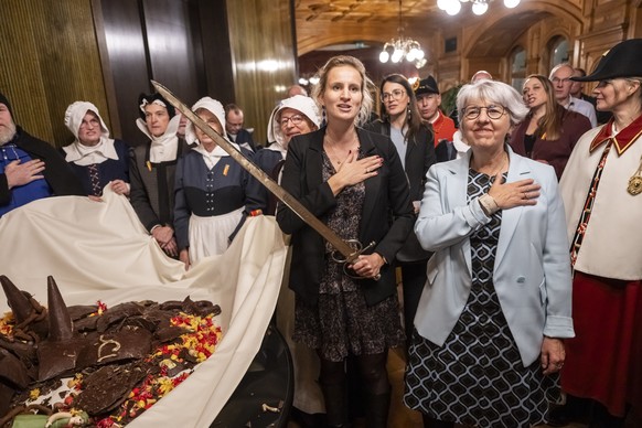 Bundesraetin Elisabeth Baume-Schneider, rechts, und die Genfer Regierungsraetin Delphine Bachmann, singen mit den Anwesenden die Hymne von Genf, nachdem sie bei der Zeremonie der Escalade den Schokola ...