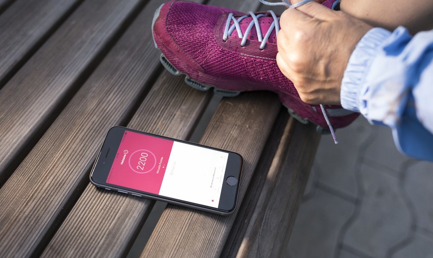 [Symbolbild / Gestellte Aufnahme] Eine Frau schnuert die Schnuersenkel ihrer Turnschuhe waehrend ein Smartphone mit der Helsana+ App daneben liegt, aufgenomen am 25. Oktober 2017 in Zuerich. Um die Sc ...