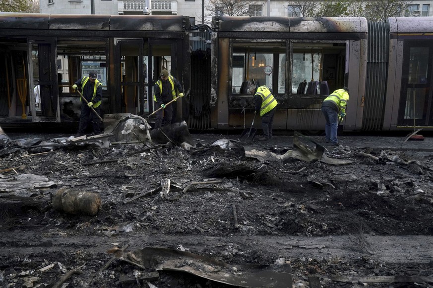 Debris is cleared from a burned out Luas and bus on O&#039;Connell Street, in the aftermath of violent scenes in the city centre on Thursday evening, in Dublin, Friday, Nov. 24, 2023. The unrest came  ...