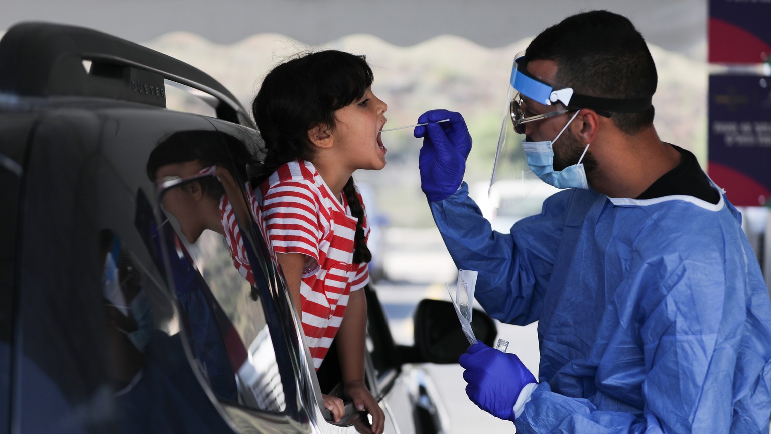 epa09446068 Medical staff takes a sample from an Israeli child at a coronavirus test and drive complex in Jerusalem, 03 September 2021. As number of Covid-19 infections among children up to the age of ...