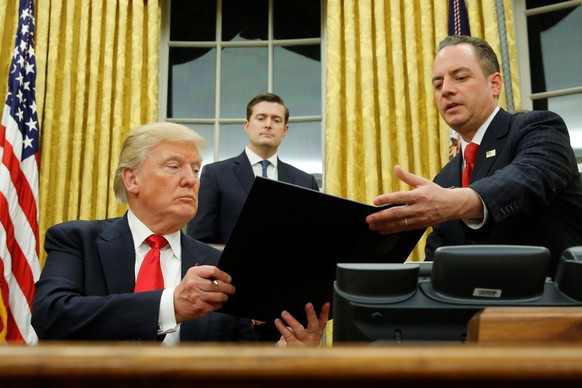 U.S. President Donald Trump hands Chief of Staff Reince Priebus (R) an executive order that directs agencies to ease the burden of Obamacare, after signing it in the Oval Office in Washington, U.S. Ja ...