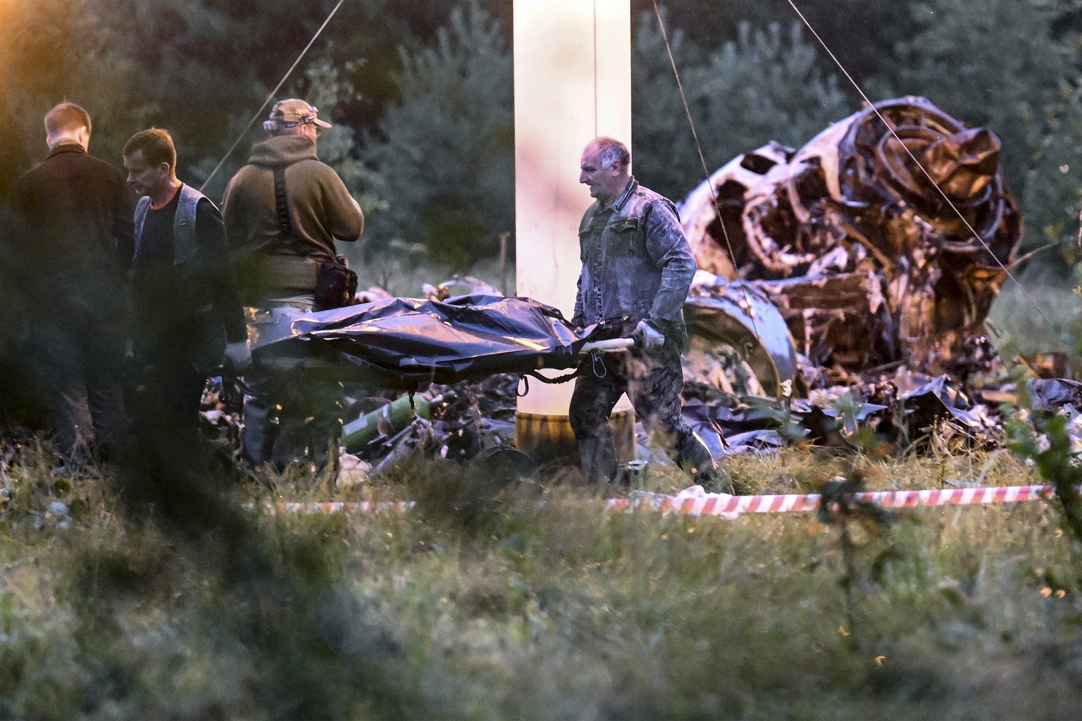 FILE - People carry a body bag away from the wreckage of a crashed private jet, near the village of Kuzhenkino, Tver region, Russia, on Aug. 24, 2023. Yevgeny Prigozhin dies exactly two months after t ...