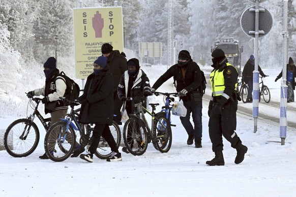 A Finnish border guard, right, walks with migrants with two bicycles at the international border crossing at Salla, northern Finland, on Tuesday, Nov. 21, 2023. Finland, which joined NATO this year in ...