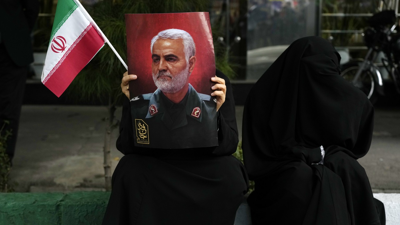 A protester holds a poster of the late Iranian Revolutionary Guard General Qassem Soleimani, who was killed in a US drone strike in 2020, and an Iranian flag during a rally for the former US.