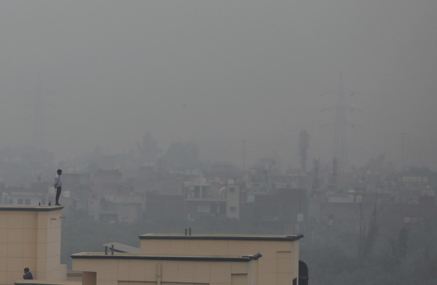 A man is seen standing on the ledge of a building as smog envelopes the horizon in New Delhi, India, Thursday, Dec. 2, 2021. (AP Photo/Altaf Qadri)