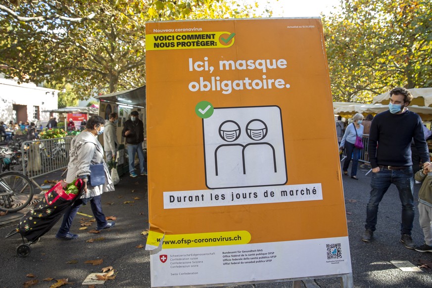 epa08770135 Customers wearing protective face masks against the spread of the coronavirus COVID-19 passe near a sign with instruction reading &#039;Here, face mask is mandatory&#039; at the market, in ...