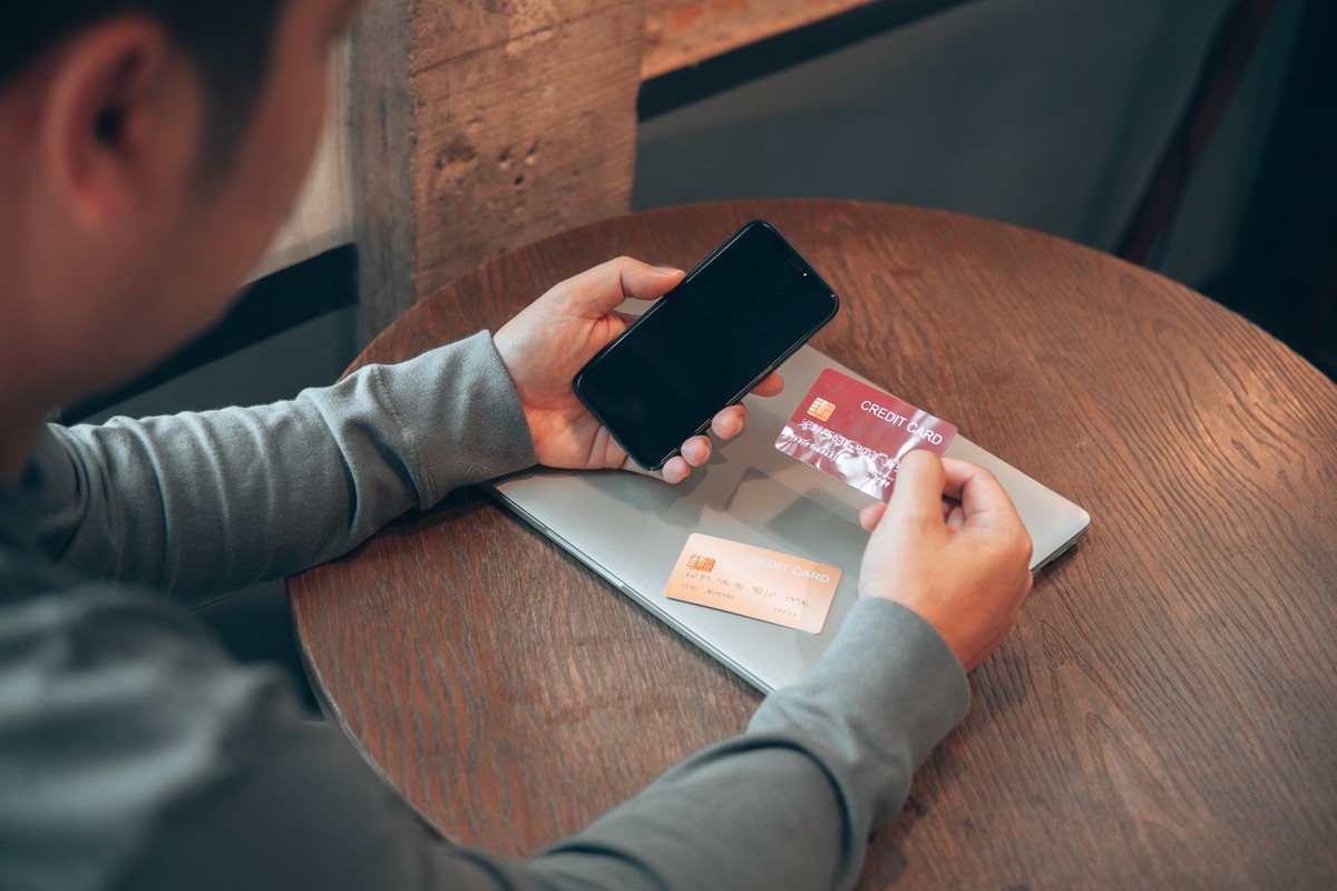 Rear view over shoulder, Man holding mobile phone and choosing credit card for internet banking. Credit card payment for online shopping. Concerned for Mobile App network security.
