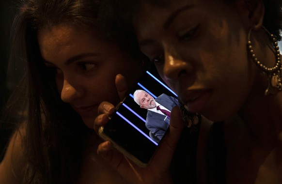Women listen on a mobile phone to an interview of former president Luiz Inacio Lula da Silva, who is running again for president, with Jornal Nacional on TV Globo, outside a bar in Rio de Janeiro, Bra ...