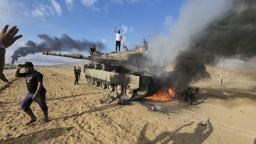 Palestinians celebrate by a destroyed Israeli tank at the Gaza Strip fence east of Khan Younis on Saturday, Oct. 7, 2023. The militant Hamas rulers of the Gaza Strip carried out an unprecedented, mult ...