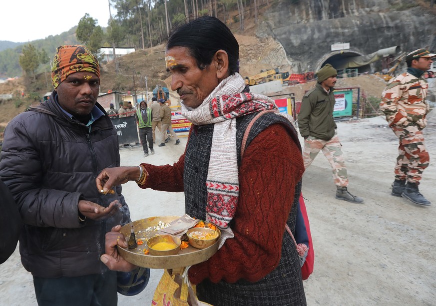 epa10997160 A local Hindu priest (C) distributes offerings to a worker arriving at the site of the Silkyara tunnel that collapsed while being under construction, to join in rescue operations, in Uttar ...