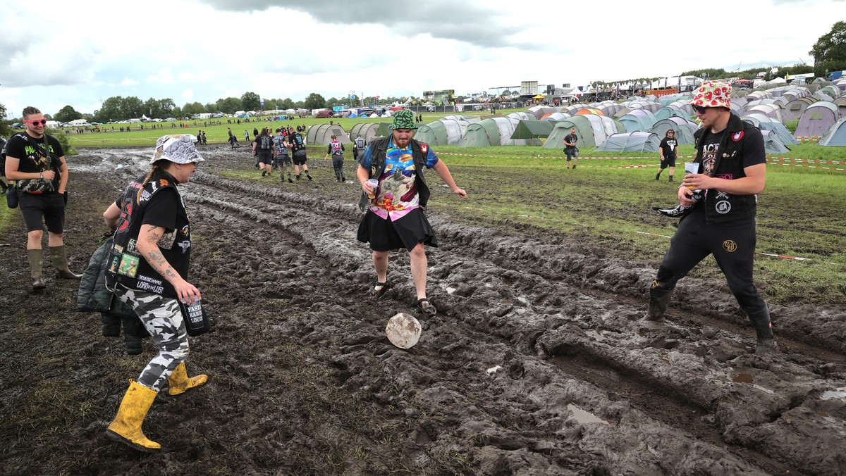 01.08.2023, Schleswig-Holstein, Wacken: Metal-Fans spielen auf dem vom Regen aufgeweichten und schlammigen Festivalgel