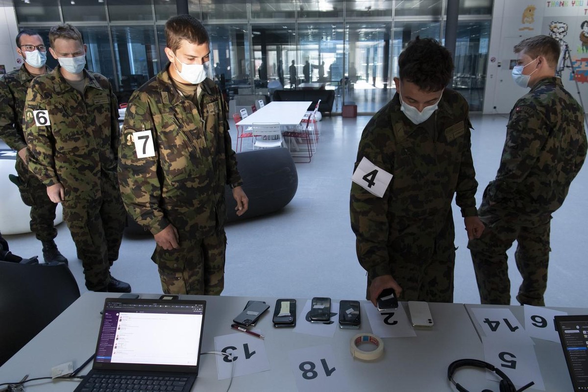 Des soldats de l'armée suisse portant un masque de protection prennent un smartphone sur une table avec l'application à l'aide du traçage de proximité décentralisé préservant la confide ...