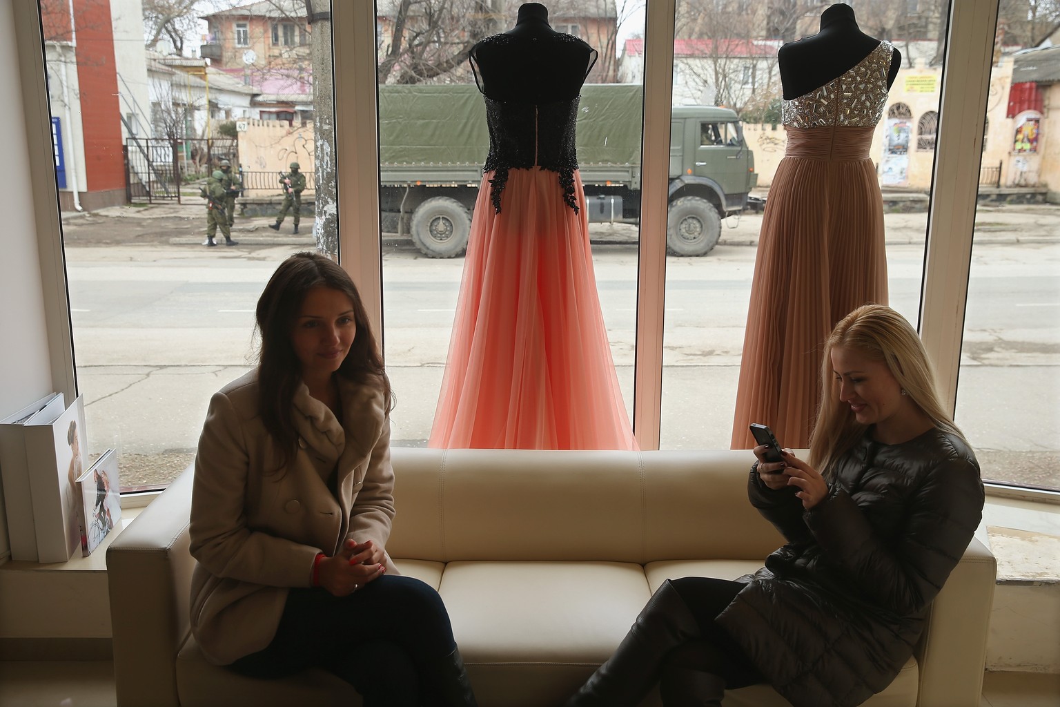 Zwei junge Frauen sitzen in einem Laden mit Abendkleidern in Simferopol, draussen patrouillieren die Soldaten.