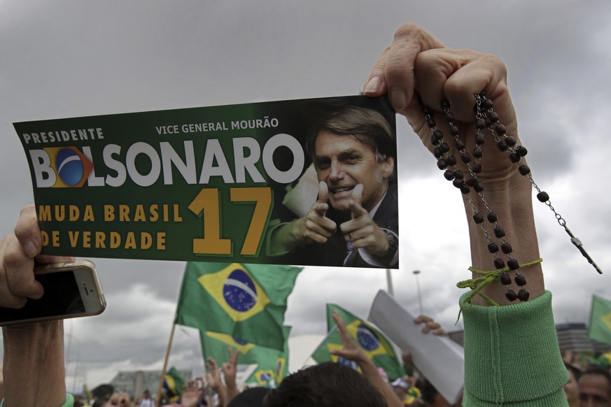 FILE - In this Oct. 21, 2018 file photo, a supporter of presidential frontrunner Jair Bolsonaro holds up a bumper sticker promoting her candidate, during a campaign rally in Brasilia, Brazil. Perhaps  ...