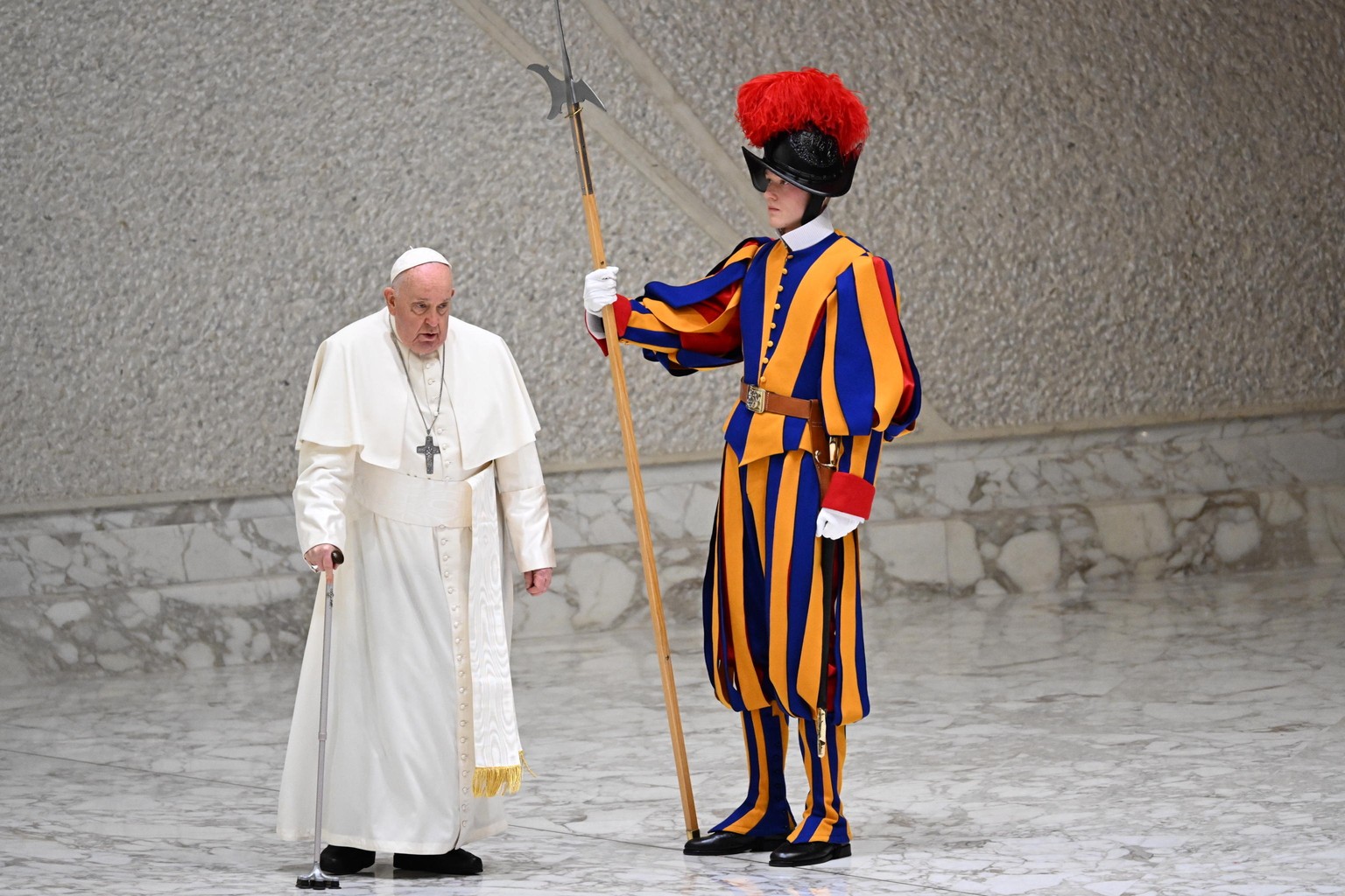 epa11067036 Pope Francis, using a cane, walks past a member of the Pontifical Swiss Guard as he arrives to lead his weekly general audience in the Paul VI Audience Hall, in Vatican City, 10 January 20 ...