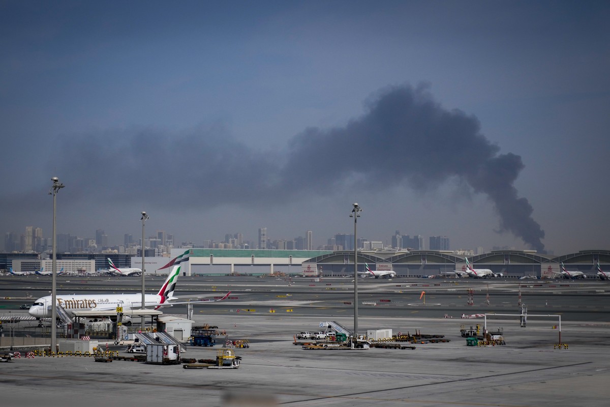 KEYPIX - A plume of smoke caused by an Iranian strike is seen in the background as Emirates planes are parked at Dubai International Airport after its closure in Dubai, United Arab Emirates, Sunday, M ...