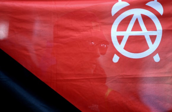 epa06069142 A protester is seen behind a banner showing an anarchist symbol as he arrives at Hamburg Hauptbahnhof central railway station ahead of the G20 Summit in Hamburg, Germany, 06 July 2017. The ...