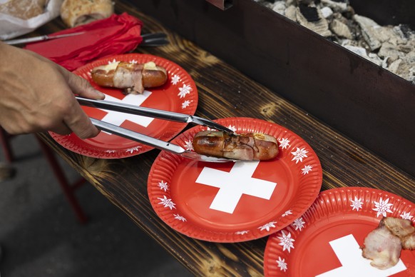 Ein Besucher legt einen gegrillten Cervelat auf einen Pappteller mit einem Schweizer Kreuz, waehrend der Bundesfeier am Freitag, 1. August 2025 auf dem Bundesplatz in Bern. (KEYSTONE/Peter Klaunzer)