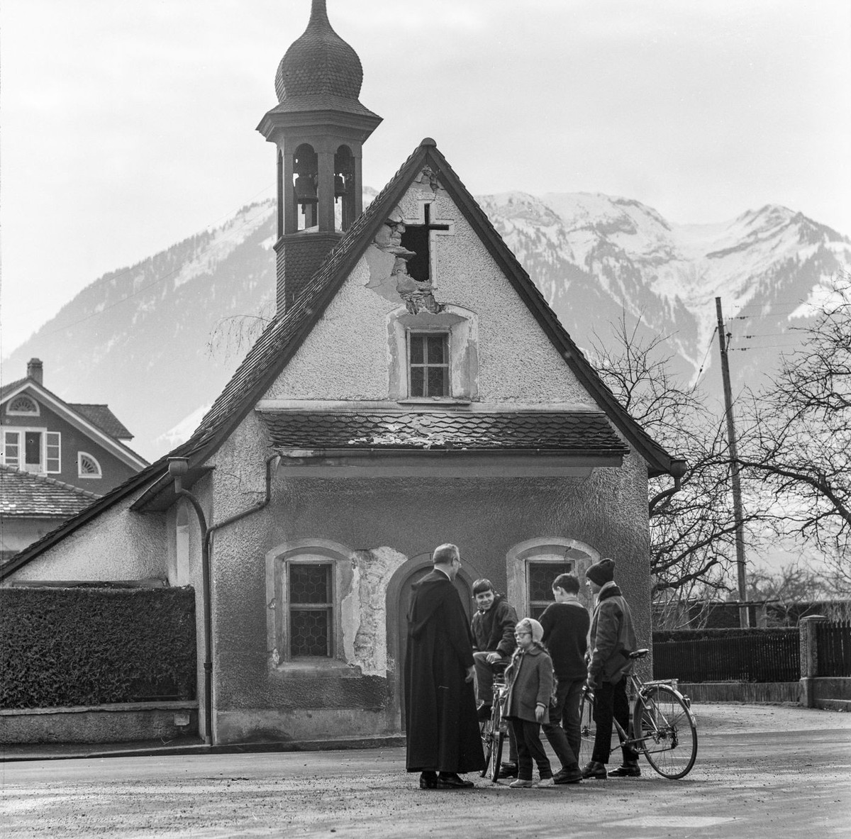 Ein Geistlicher mit Kindern vor der beschaedigten St. Antonia- Kapelle von Sarnen, Kanton Obwalden nach dem starken Erdbeben am 14. Maerz 1964. Anfang 1964 hielten Erdstoesse den Kanton Obwalden woche ...