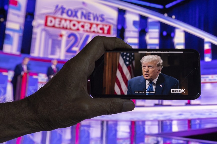 epa10816789 A viewer watches the first Republican presidential debate live on Fox News and former President and candidate Donald Trump&#039;s interview by Tucker Carlson on the platform &#039;X&#039;  ...