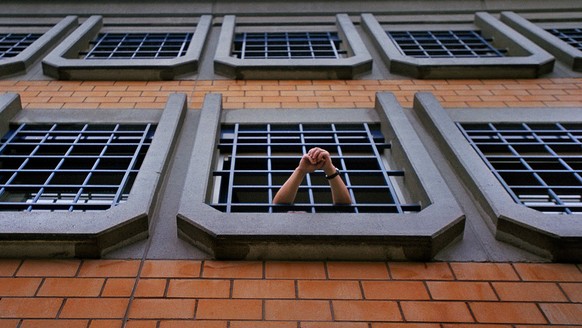 Ein Haeftling der Kantonalen Strafanstalt Poeschwies in Regensdorf (ZH) hat am 15. Dezember 2003 das Fenster seiner Zelle geoeffnet und stuetzt seine Arme auf dem Gitter ab. (KEYSTONE/Gaetan Bally) :  ...