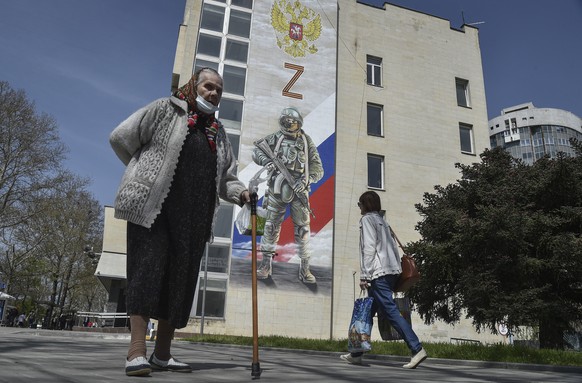 epa09910306 Pedestrians pass a mural depicting a Russian soldier, the Russian flag and double-headed eagle coat of arms as well as the &#039;Z&#039; military symbol, on the side of a building in Simfe ...