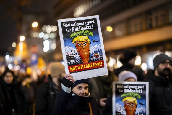 epa12662386 A protester holds a placard showing a caricature of US President Donald Trump and reading 'Not welcome to here!' during a rally against the World Economic Forum (WEF) and the vis ...