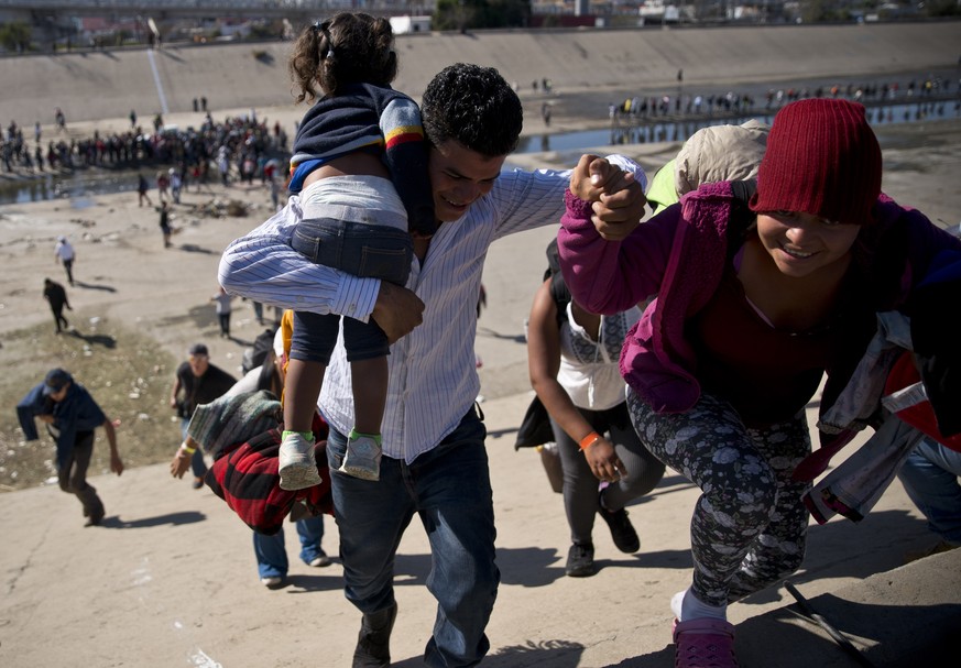 Migrants walk up a riverbank at the Mexico-U.S. border after getting past a line of Mexican police at the Chaparral border crossing in Tijuana, Mexico, Sunday, Nov. 25, 2018, as they try to reach the  ...