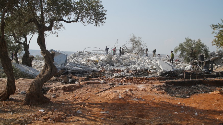 epa07955650 People walk on rubble at the site that was hit by helicopter gunfire which reportedly killed nine people, including Abu Baker al-Baghdadi, the leader of IS or so-called Islamic State, near ...