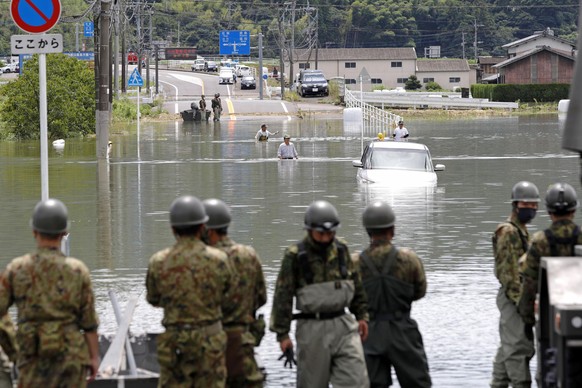 People wade through a flooded road after torrential rain, watched by Japan Ground Self-Defense Force personnel, foreground, in Takeo, Saga prefecture, southwestern Japan, Sunday, Aug. 15, 2021. Heavy  ...