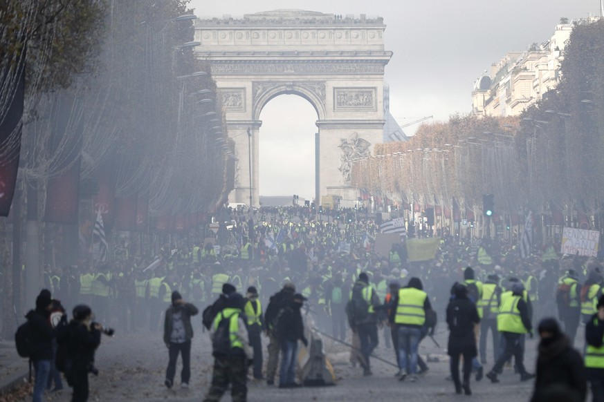 In a cloud of tear gas demonstrators, called the yellow jackets, try to set up makeshift barricades on the famed Champs-Elysees avenue in Paris, France, as they protest against the rising of the fuel  ...