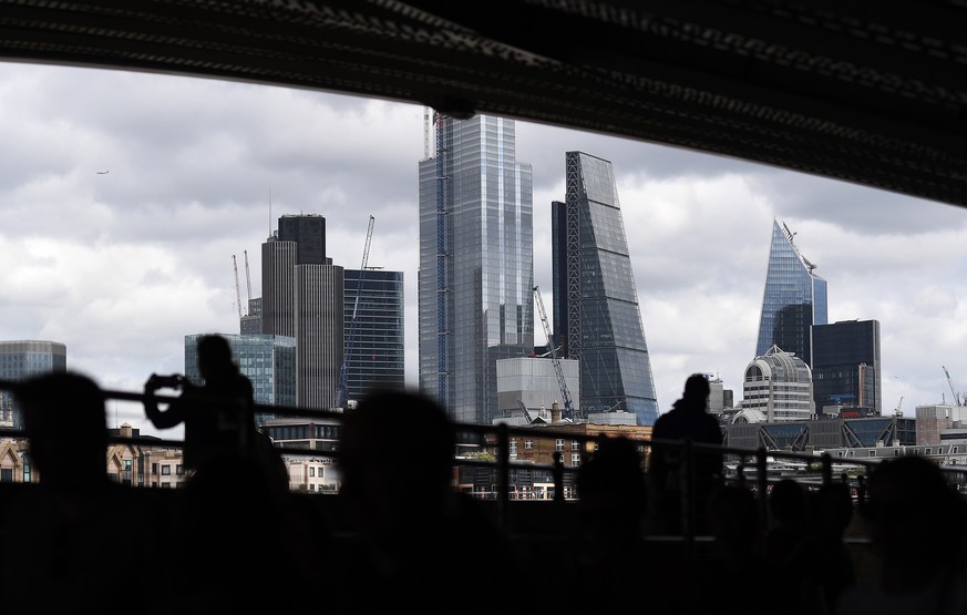 epa07764129 Pedestrians are silhouetted against the City of London in London, Britain, 09 August 2019. The British economy contracted by 0.2 percent between April and June 2019. The Pound Sterling sub ...