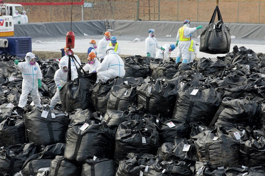 Workers pile up plastic bags containing radiation-contaminated fallen leaves and surface soil collected from surrounding area in the municipal baseball field for temporary storage in Okuma, a town whe ...