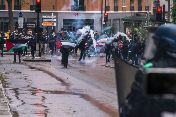 epa09202460 Protesters hold the Palestinian flags amid tear gas from riot police during clashes as part of a rally organized by several associations in support of the Palestinian people, in Paris, Fra ...