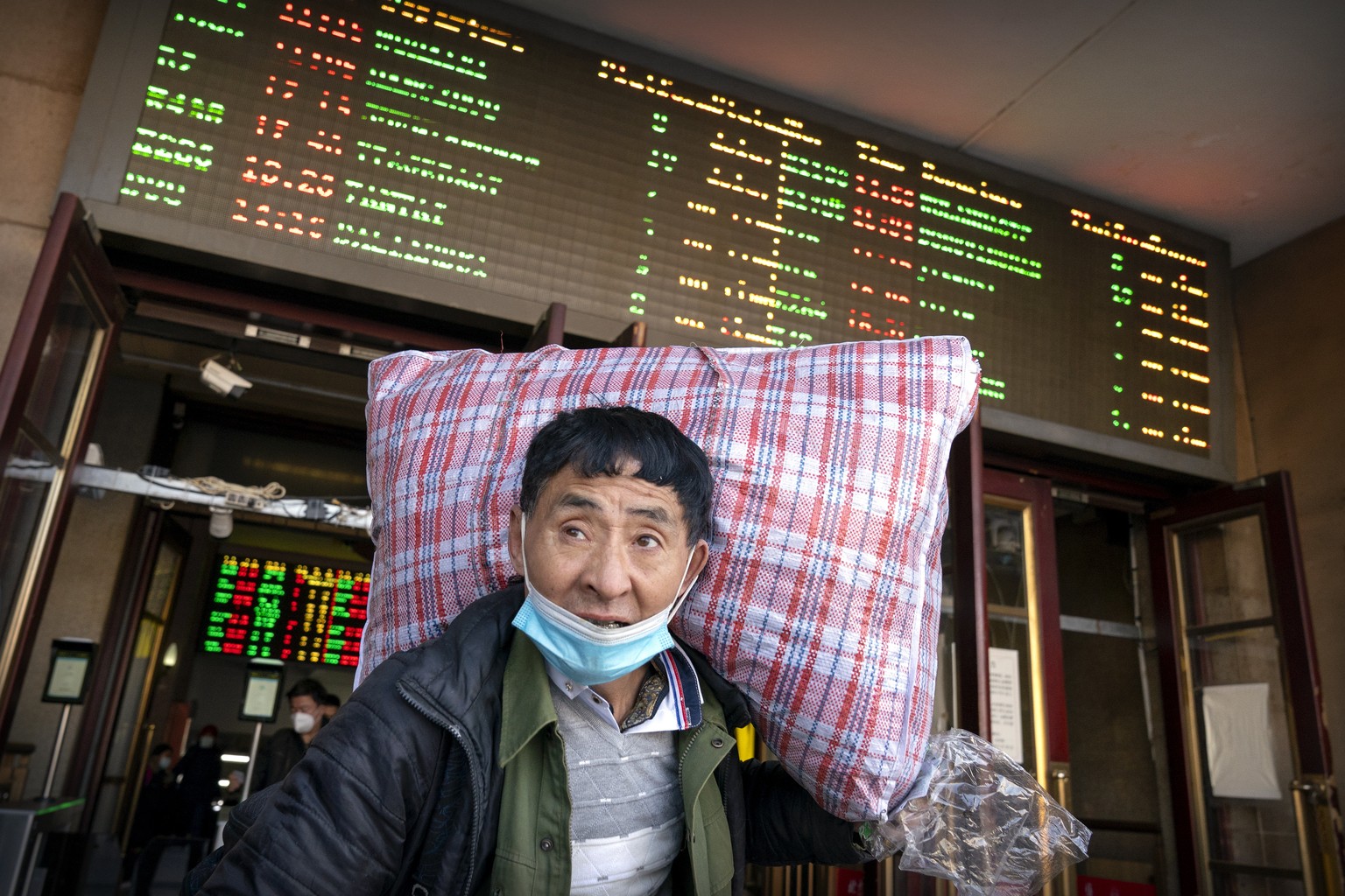 A traveler wearing a face mask to protect against the spread of the coronavirus carries his luggage as he walks out of an exit at the Beijing Railway Station in Beijing, Thursday, Jan. 28, 2021. Effor ...