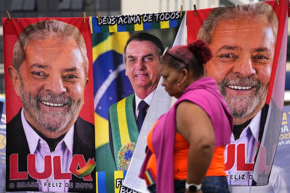 A woman walks past towels emblazoned with images of Brazilian presidential candidates, President Jair Bolsonaro, center, and former President Luiz Inacio Lula da Silva, displayed for sale by a street  ...