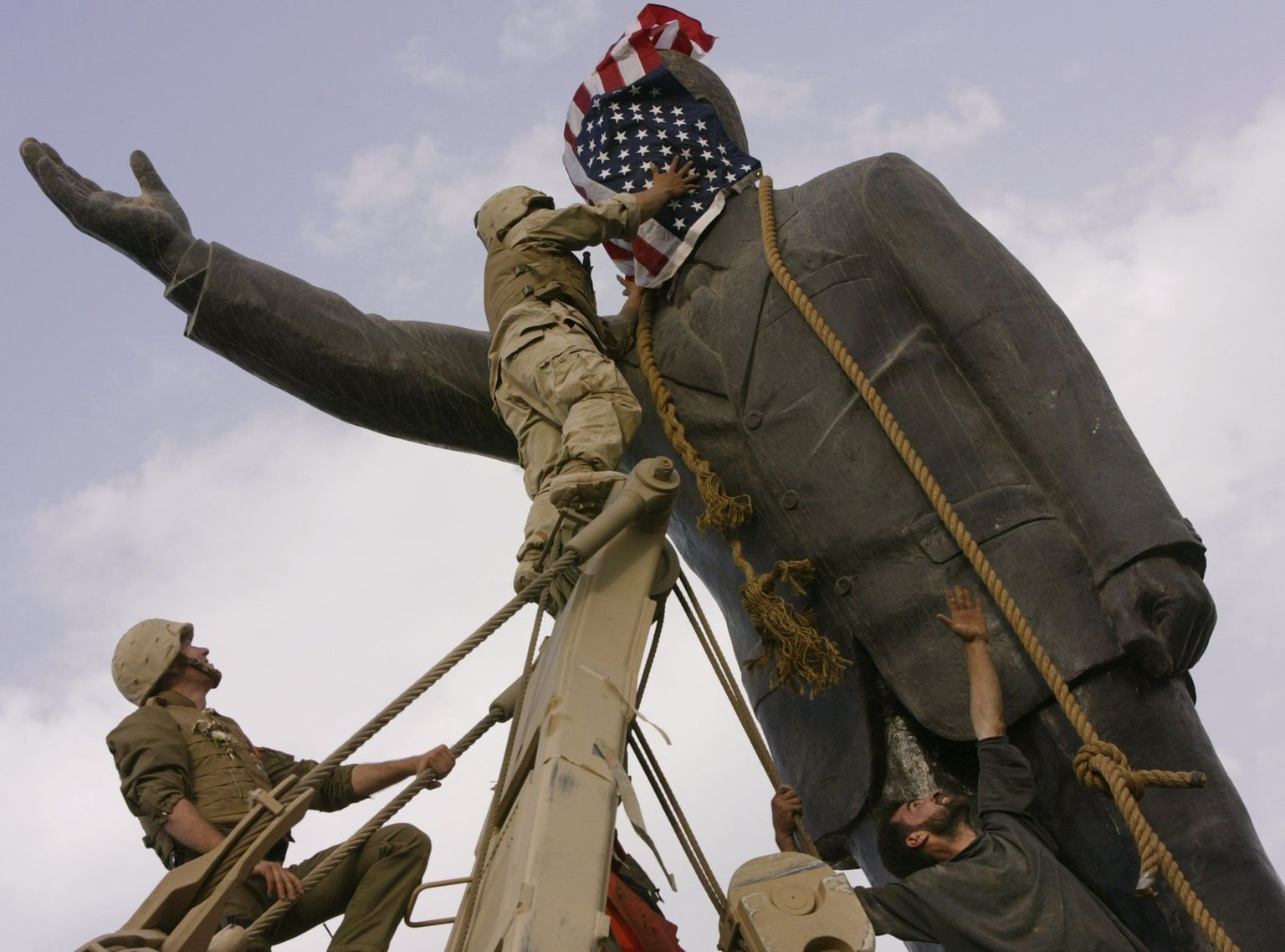 FILE - In this April 9, 2003, file photo, an Iraqi man, bottom right, watches Cpl. Edward Chin of the 3rd Battalion, 4th Marines Regiment, cover the face of a statue of Saddam Hussein with an American ...