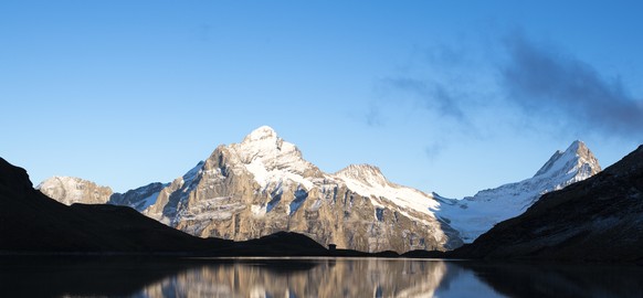 A man looks at the mountains Wetterhorn, Lauteraarhorn, Schreckhorn and Finsteraarhorn that are reflecting during the sunset in the Bachalpsee lake (2265m) close to the First, above Grindelwald in the ...