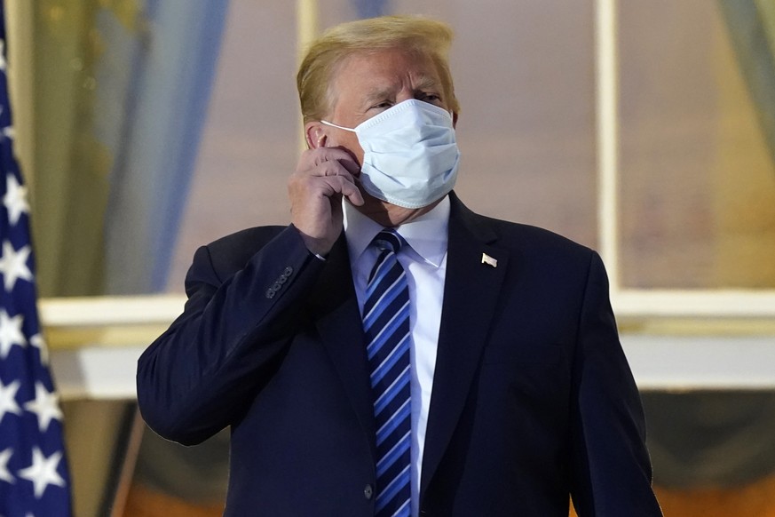 President Donald Trump removes his mask as he stands on the balcony outside of the Blue Room as returns to the White House Monday, Oct. 5, 2020, in Washington, after leaving Walter Reed National Milit ...