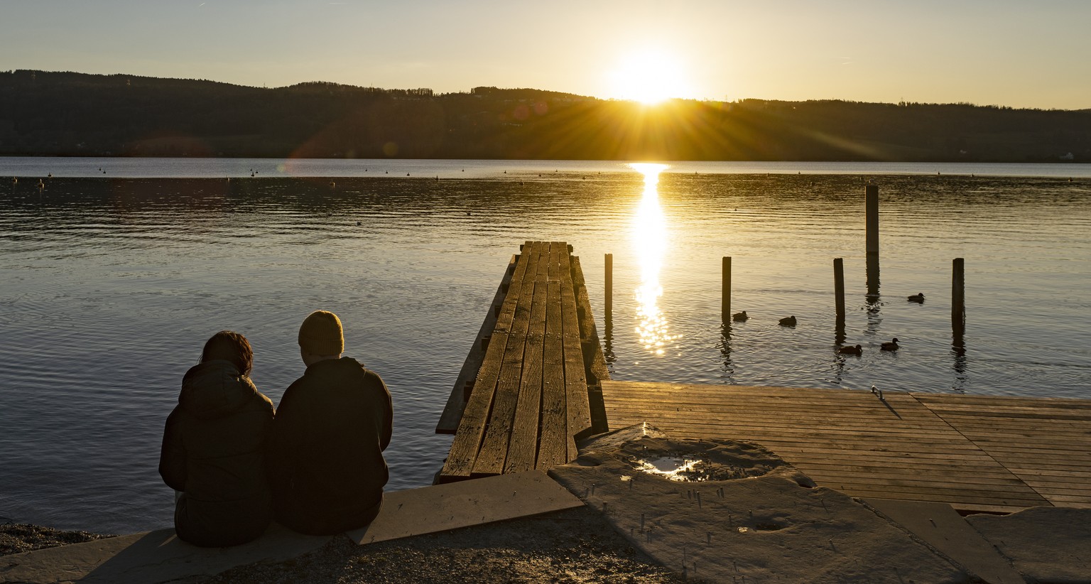 epa09787616 People watch the sunset at the Greifensee lake near Zurich, Switzerland, 26 February 2022. EPA/WALTER BIERI